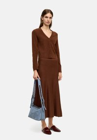 Brązowy sweter wykonany na drutach z zapięciem na guziki i długimi rękawami, zestawiony z pasującą brązową spódnicą. Niebieska torebka zamszowa z teksturowanymi akcentami.