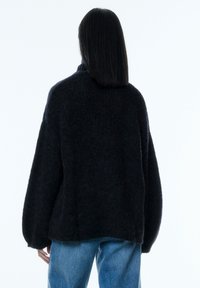 Pull noir surdimensionné avec une finition texturée, doté d'un col montant et de larges manches bouffantes. Associé à un jean bleu clair.