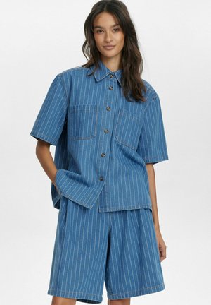 Camicia di jeans blu a maniche corte e pantaloni corti abbinati con righe verticali bianche. Presenta due tasche sul petto e una chiusura con bottoni.