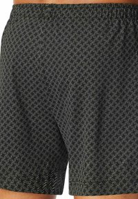 Zwarte shorts met een licht geometrisch patroon, elastische tailleband en een relaxte pasvorm. Het materiaal lijkt zacht met een gladde textuur.