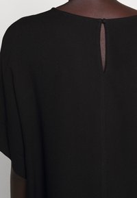 Robes noires avec une texture douce, caractérisée par un décolleté rond et un détail à trou de serrure au dos, maintenu par un petit bouton.