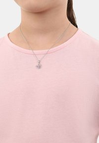 Eine silberne Kettenhalskette mit einem Herzanhänger und rosa Akzenten. Trägt man über einem hellrosa Hemd, zeigt einen einfachen, legeren Look.