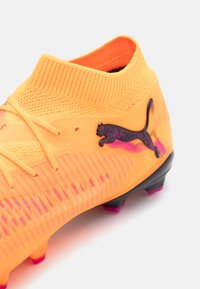 Scarpa da calcio di un brillante arancione con superficie texturizzata, logo Puma nero e dettagli in gradiente viola sulla suola e sui tacchetti.