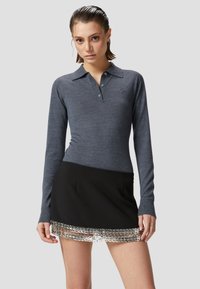 Polo a maniche lunghe in tessuto knit blu scuro con colletto e tre bottoni, abbinato a una mini gonna nera con dettagli metallici argentati.
