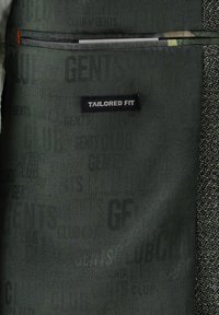 Sakko mit maßgeschneiderter Passform aus dunkelgrünem Stoff mit dezenten Textmustern, einem kontrastierenden Gewebe rechts und einer Reißverschlusstasche.