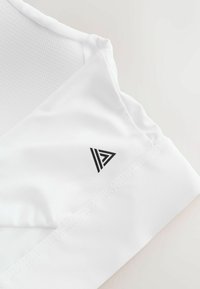 Vêtement de sport en tissu blanc avec un petit logo géométrique noir comprenant trois lignes parallèles formant un triangle stylisé près de la couture de l'épaule.