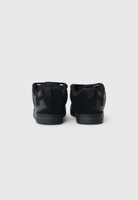 Zapatillas negras con parte superior de gamuza texturizada y malla, con un logotipo negro prominente en el talón y una suela de goma sólida.