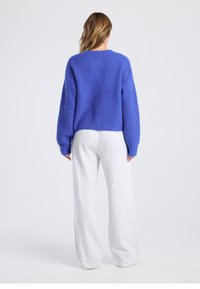 Blue knitted sweater with a textured pattern, loose fit, and long sleeves, paired with light grey, wide-leg sweatpants.