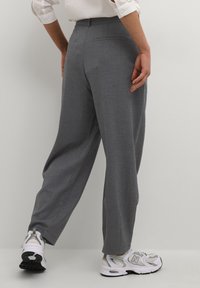 Pantalons gris ajustés à coupe droite, avec une texture lisse et un motif subtil, associés à des baskets de sport blanches et grises.