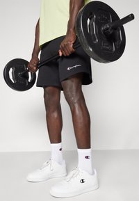 Black Champion shorts, white Champion sneakers, and white athletic socks. Holding a black barbell with weights. Light green shirt.