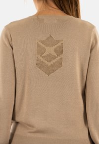 Maglione beige lavorato a maglia con un grande motivo a stella e scudo testurizzato sulla parte posteriore, caratterizzato da un collo a giro e un orlo a coste.
