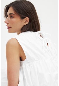 Vit ärmlös blus med samlad midja, med en knytdetalj bak och ett mjukt, lätt material.