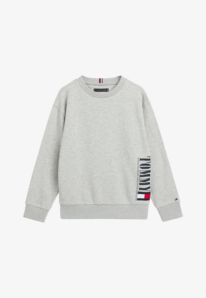 Sweat-shirt gris clair à col rond avec poignets et ourlet côtelés, avec un texte vertical "TOMMY" et un logo drapeau sur le côté droit près de l'ourlet.