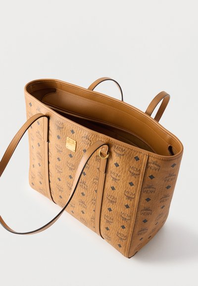 Sac cabas MCM en cuir fauve avec motif logo noir, deux poignées et ouverture sur le dessus montrant un compartiment intérieur à fermeture éclair.