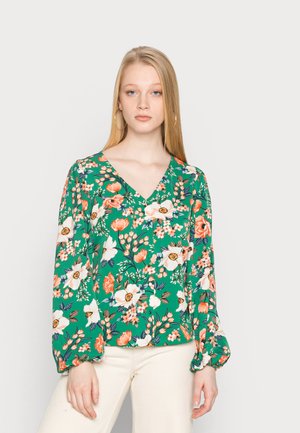 Blusa floral em tecido verde com decote em V, mangas longas volumosas e uma vibrante mistura de flores laranja, brancas e amarelas por todo o tecido.