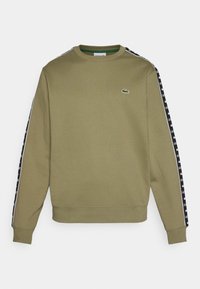 Sudadera verde oliva con cuello redondo, que presenta paneles laterales negros decorados con texto de logotipo blanco y un pequeño logotipo de cocodrilo bordado.