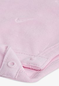 Svetlo roza bombažno blago z mehko teksturo, z všitim robom in dvema plastičnima pritrdilnima gumboma na izrezu za zapiranje.