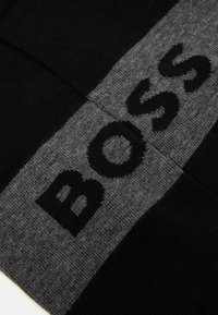 Sciarpa a maglia nera e grigia con il logo audace "BOSS" in nero. Texture liscia con blocchi di colore a contrasto, che enfatizzano la prominenza del marchio.