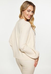 Cardigan crema a coste con una vestibilità rilassata, maniche lunghe e orlo leggermente corto. Texture morbida e design semplice.