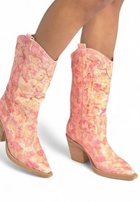 Botas de vaquero rosas con una textura veteada, puntera afilada y costuras decorativas. Presentan un tacón de madera apilada y un borde superior en forma de onda.