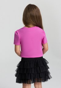 T-shirt rosa di cotone a maniche corte con scollatura rotonda, abbinato a una gonna di tulle nera con più strati arricciati.