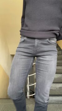 Άτομο που φοράει σκούτερο πουλόβερ και γκρι τζιν κατεβαίνει εσωτερικές σκάλες με μπεζ τοίχο και λευκή κουπαστή στο φόντο.