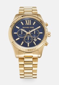 Gold-tone chronograph watch by Michael Kors. Features a navy dial, gold hour markers, and a link bracelet. Date display is visible at 4 o'clock.