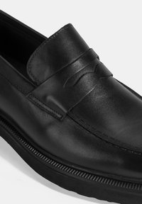 Zwarte leren loafers met een gladde textuur, voorzien van een gestikte penny strap accent en een subtiel verhoogd ontwerp op de bovenkant. Rubberen zool.