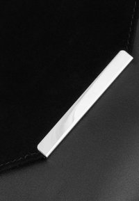 Črna usnjena tekstura s sijajno srebrno pravokotno kovinsko dekoracijo. Oblikovanje je elegantno in minimalistično, s čistimi linijami in šivi.