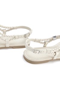 White braided sandals featuring a flat design, adjustable ankle strap with silver hardware, and a textured matte upper.