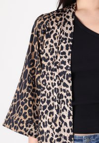 Kimono con stampa leopardata in tonalità nere e beige; presenta maniche ampie e un tessuto leggero; indossato sopra una maglietta nera a costine.