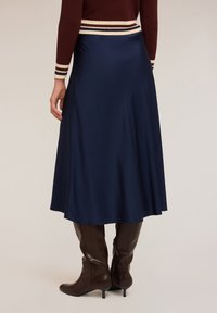 Fustă midi din satin albastru marin cu o textură netedă, strălucire subtilă și un design evazat, asortată cu cizme din piele maro până la genunchi.