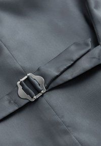 Primo piano di una cintura in tessuto grigio scuro con fibbia rettangolare argentata fissata su un capo su misura abbinato.