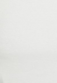 Top branco em tecido canelado com um padrão texturizado e riscas verticais, feito de um material suave, com um design ajustado.