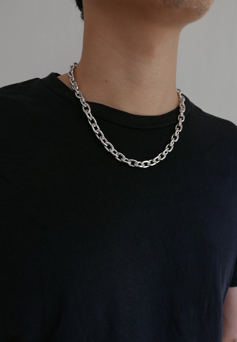 Ασημί μεταλλική αλυσίδα κολιέ με οβάλ συνδέσμους, φορεμένη πάνω από ένα μαύρο μπλουζάκι, με γυαλιστερή φινίρισμα και μέτριο πάχος.