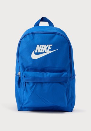 Sinine nailonist seljakott, millel on ees lukuga tasku ja suur valge Nike logo. Sellel on pehmed õlarihmad ja ülaosas kandekäepide.