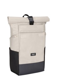Sac à dos roll-top beige clair avec un fond noir. Il dispose d'une sangle ajustable, d'une poche avant avec Velcro et d'une étiquette de marque. Tissu durable.