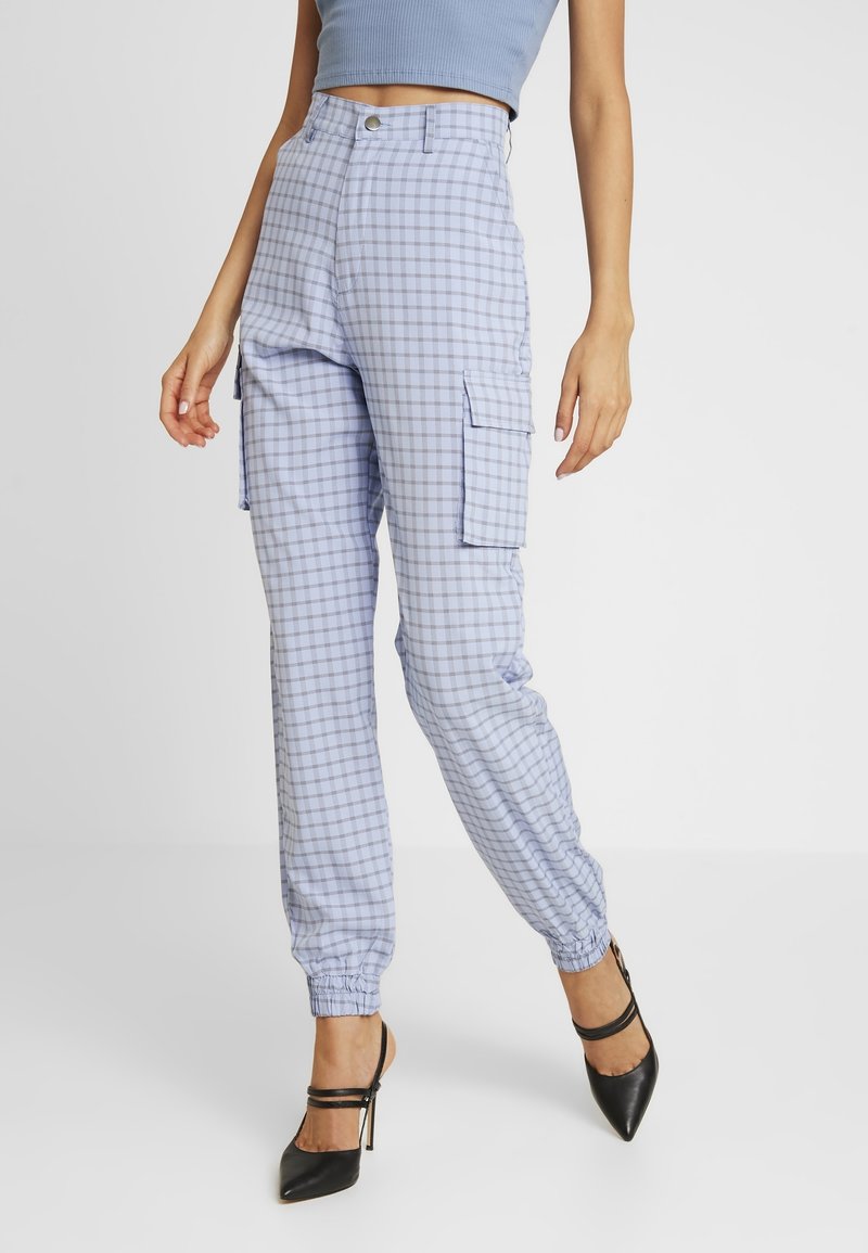 Femme portant un pantalon cargo bleu à carreaux taille haute avec des poignets élastiques et des talons noirs à bout pointu.