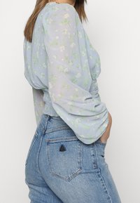 Blommig blus i ljusblått med gröna accenter, puffärmar och rynkiga detaljer, ihop med högmidjade, blekta blå denimshorts.