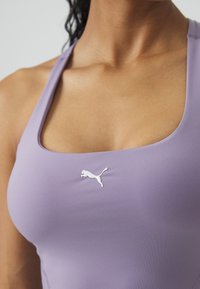 Gros plan d'une personne portant un haut de sport sans manches lavande avec un logo Puma blanc centré sur la poitrine.