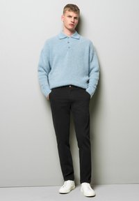 Lichtblauwe, fluffy sweater met een kraag en drie knopen, gecombineerd met zwarte broek en witte sneakers. Eenvoudig, ontspannen ontwerp.