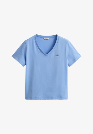 T-shirt bleu clair à col en V et manches courtes, avec petit logo brodé sur le côté gauche de la poitrine et une étiquette GANT à l'intérieur du col.
