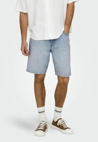 Shorts din denim de un albastru deschis, cu croial�ă dreaptă, tivuri desfăcute și design clasic cu cinci buzunare, asortați cu o cămașă albă cu nasturi și teniși maro.