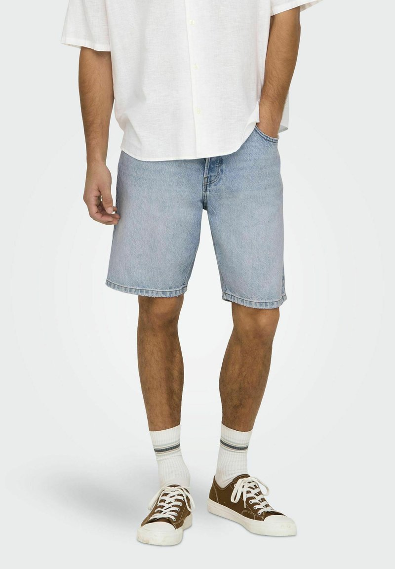 Shorts din denim de un albastru deschis, cu croială dreaptă, tivuri desfăcute și design clasic cu cinci buzunare, asortați cu o cămașă albă cu nasturi și teniși maro.