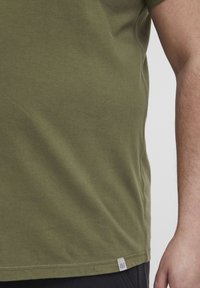 Olivengrøn t-shirt lavet af blødt bomuld. Har en rund halsudskæring, korte ærmer og et lille mærke ved kanten. Glat tekstur.
