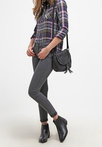 Camisa de franela a cuadros con patrones en azul, rojo y amarillo, jeans gris ajustados y botas negras hasta el tobillo. Incluye un pequeño bolso negro cruzado.