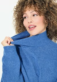 Blauer, gestrickter Rollkragenpullover. Verfügt über eine gerippte Textur, einen oversized Schnitt und einen rollierenden Kragen mit sichtbaren Stickdetails.