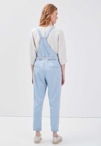 Salopette in denim blu chiaro con bretelle regolabili, vestibilità dritta e cintura intrecciata. Presenta tasche posteriori e orli ripiegati.