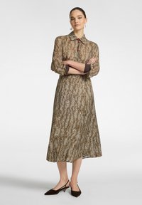 Abito marrone con stampa leopardata, colletto, bottoni rossi, maniche lunghe, dettagli marroni ai polsini e una gonna fluente. Scarpe marroni completano l'outfit.