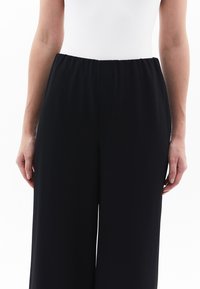 Pantaloni neri a gamba larga con cintura elasticizzata, realizzati in tessuto morbido. Il design presenta una silhouette pulita e minimale.
